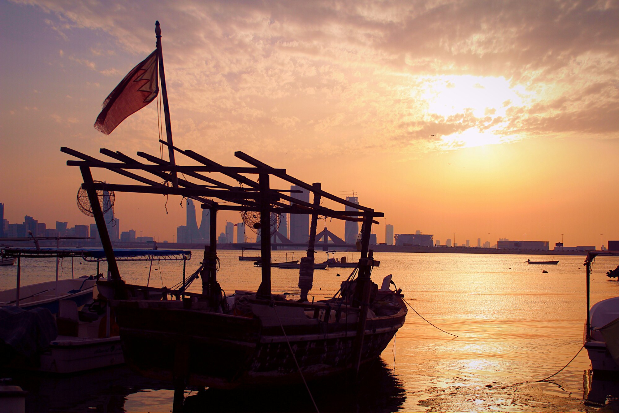 An old ship with Bahrain’s flag in front of the city and the sunset